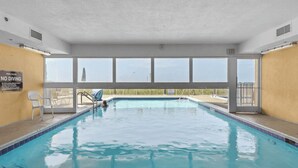 An indoor swimming pool with clear glass walls, a pool rules sign, and a view of the outside.