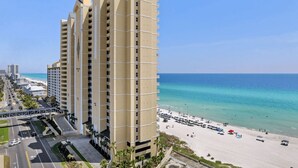 A high-rise hotel with multiple floors, a beach view, and a parking area in front.
