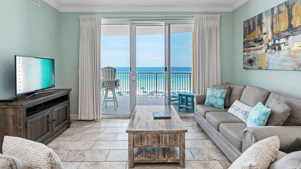 A living room with a television, a wooden coffee table, a sofa, and a view of the ocean through a sliding glass door.