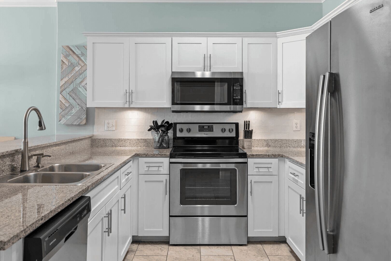 Una cocina moderna con gabinetes blancos, electrodomésticos de acero inoxidable, encimera de granito y lavavajillas.