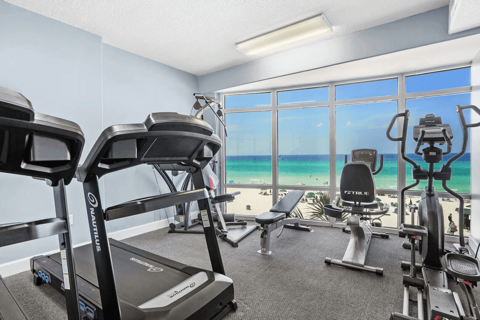A gym with Nautilus equipment, a bench, and a view of the beach.