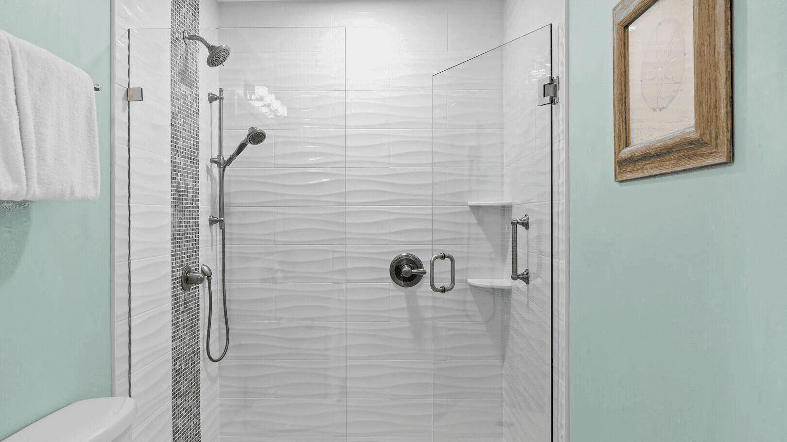 A shower with a glass door, a towel hanging on the wall, and a framed picture.