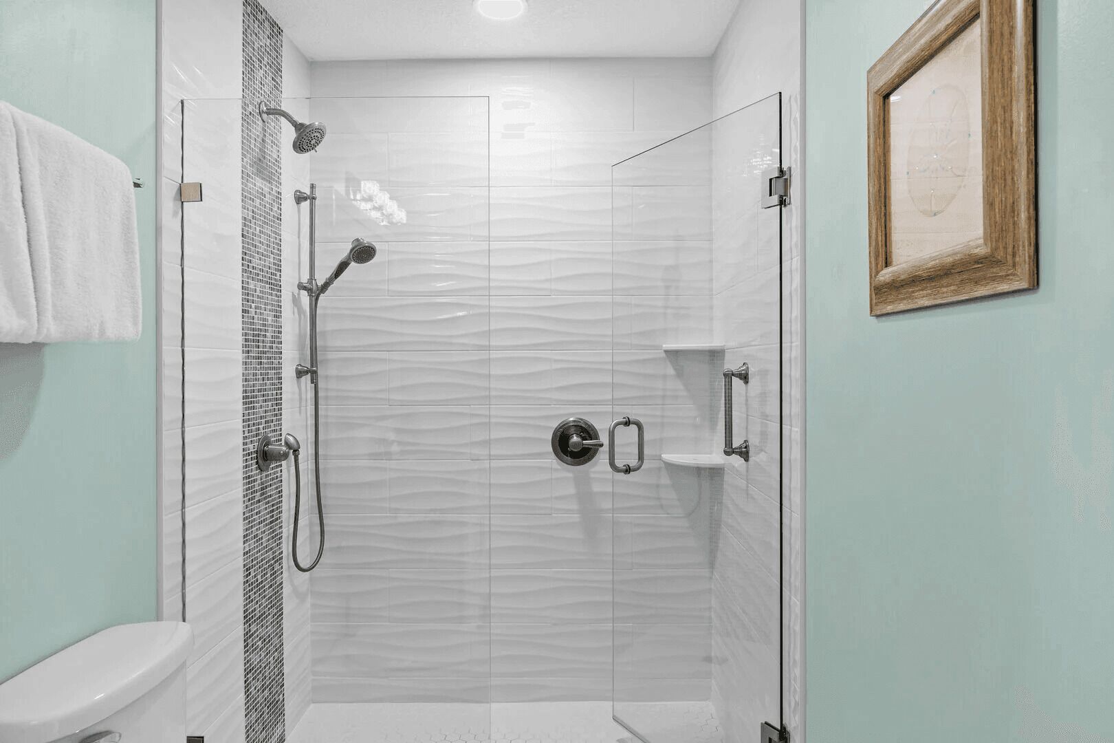 A modern bathroom with a glass-enclosed shower, a toilet, and a framed picture on the wall.