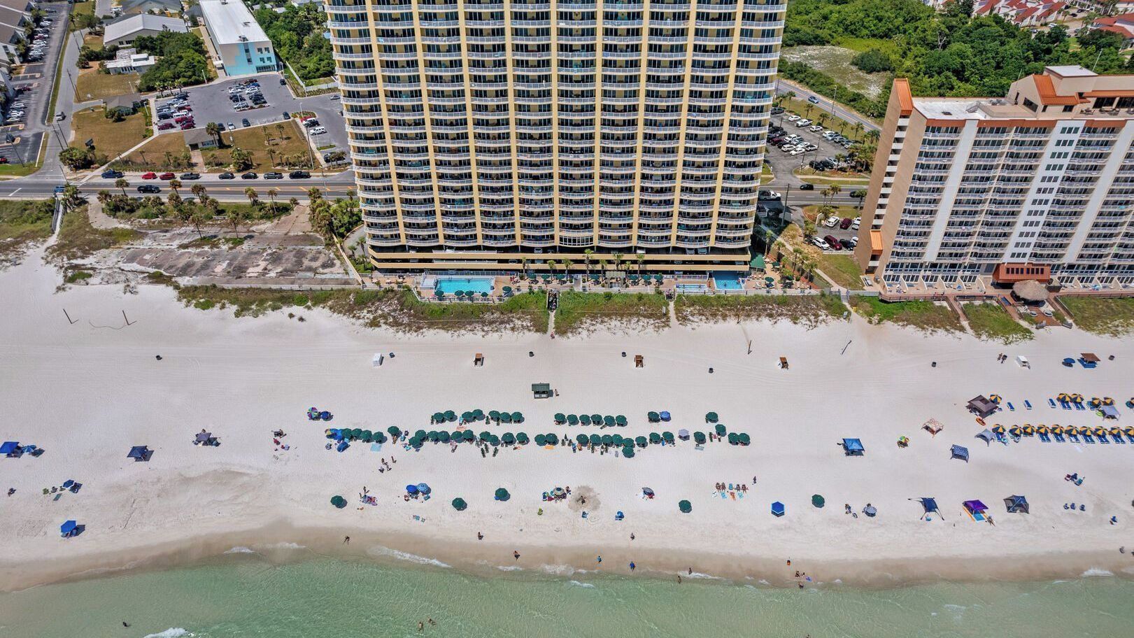 Um hotel moderno com várias varandas, uma praia com guarda-sóis e uma área de piscina.