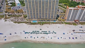 Un hotel de altura con varios balcones, una playa con sombrillas y una zona de piscina.