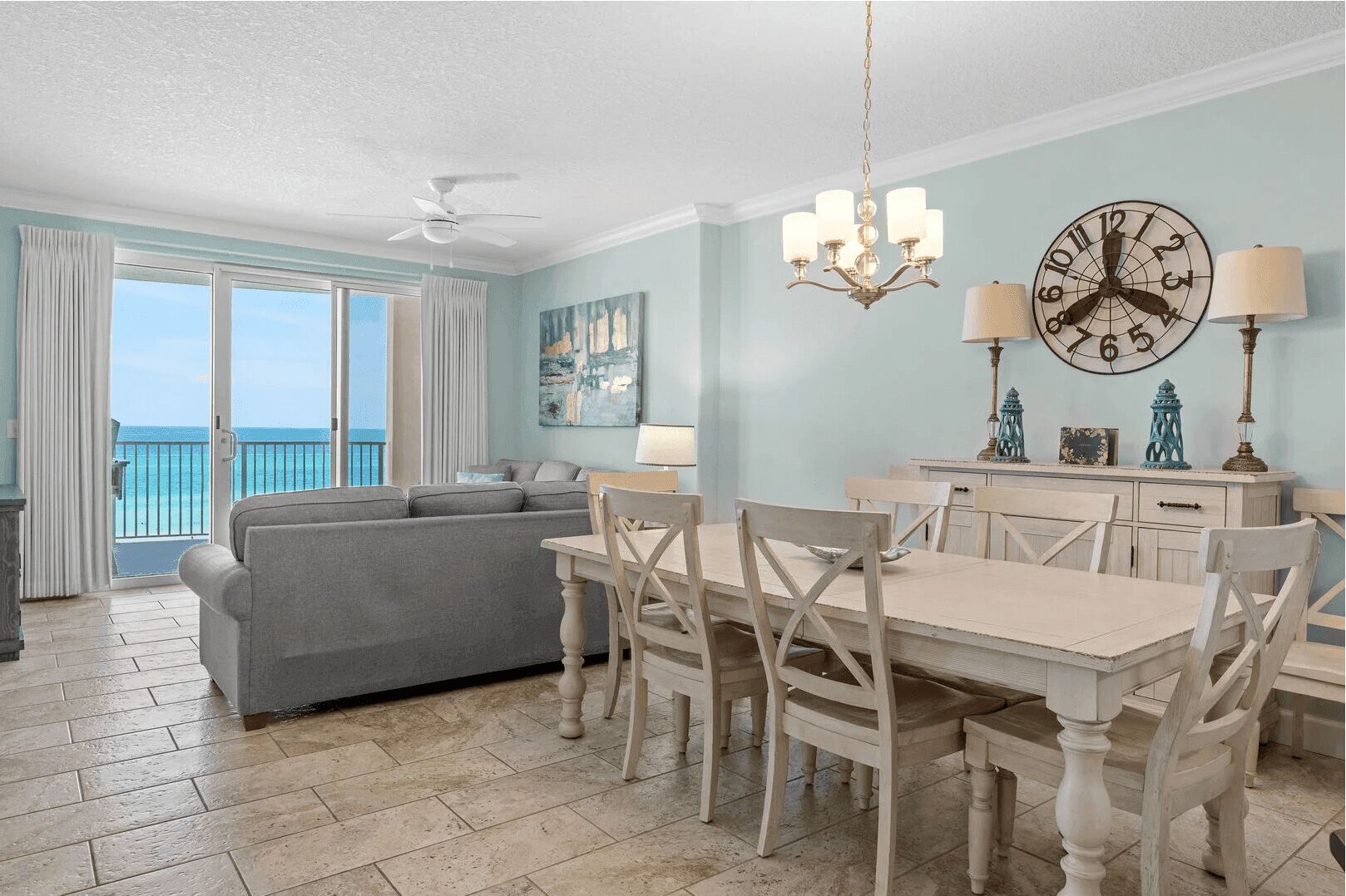 A dining area with a white table and chairs, a chandelier, and a wall clock.