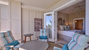 A sunlit patio with striped chairs and a round table, a bedroom with a bed and pillows, and a sign listing beach names. - Hello 30a! by Avantstay Private Beach Access + Shared Pool (Santa Rosa Beach)