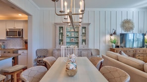 A dining area with a white table, wicker chairs, a chandelier, and a cabinet with dishes.