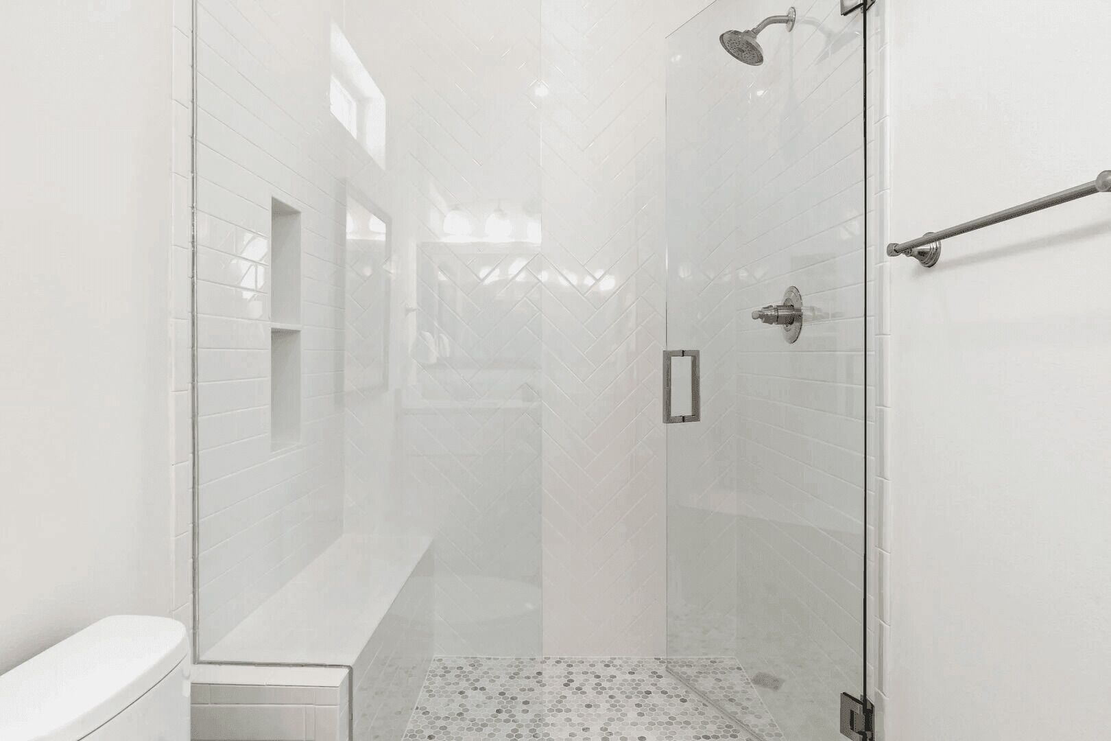 Une salle de bain moderne avec une douche à l’italienne en verre, des murs recouverts de carreaux blancs et un banc.