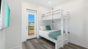A bunk bed room with a door leading to a balcony, white walls, and a wooden floor. - Wanderlust by Avantstay Walk to Beach + Pool New Construction (Panama City Beach)