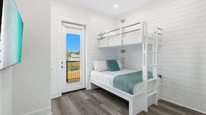 A bunk bed room with a door leading to a balcony, white walls, and a wooden floor.