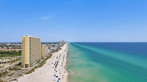 Un hotel costero con vista a la playa, varios pisos y una extensa orilla marítima.