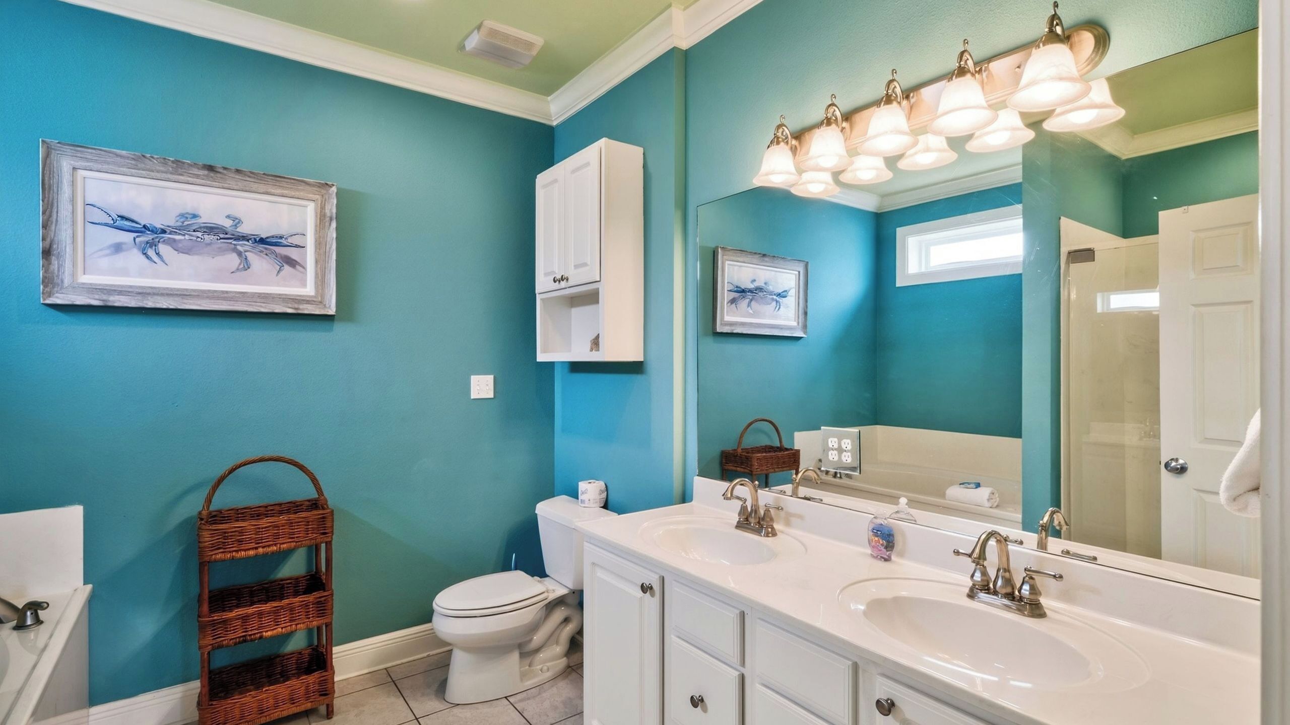 A bathroom with a white sink, a toilet, a wicker basket, and two framed pictures on the wall.