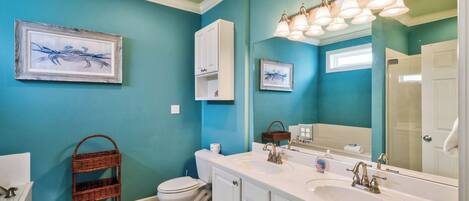 A bathroom with a white sink, a toilet, a wicker basket, and two framed pictures on the wall.