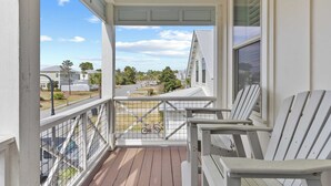 Ein überdachter Balkon mit weißen Geländern, zwei Adirondack-Stühlen und Blick auf eine Wohnstraße.