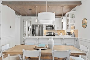 A modern kitchen with white cabinetry, stainless steel appliances, and a wooden dining table with white chairs. - Sun by Avantstay Gulf Place Golf Cart, Pool, Bikes (Santa Rosa Beach)