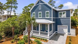 A two-story house with a porch, a garage, and a well-maintained garden. - Cabana Blue by Avantstay Walk to Beach, Golf Cart+bikes Included Pool Access (Santa Rosa Beach)