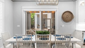 A dining area with a white table and chairs, a hanging light fixture, and a view through glass doors to an outdoor space. - Cabana Blue by Avantstay Walk to Beach, Golf Cart+bikes Included Pool Access (Santa Rosa Beach)