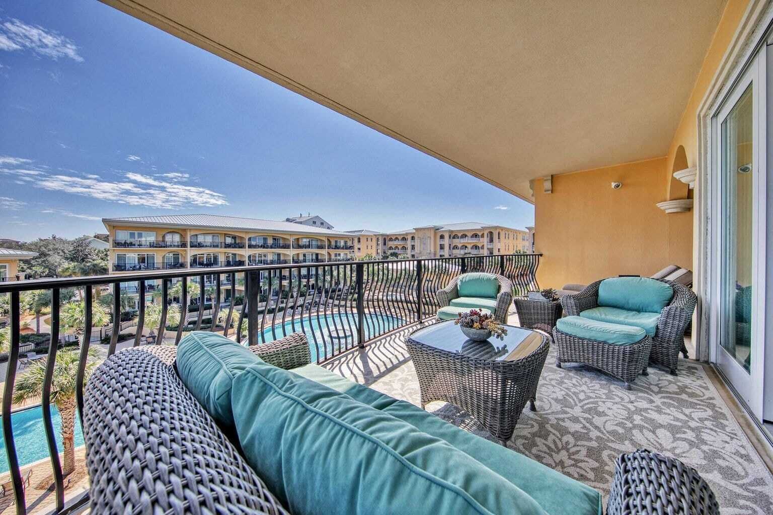 Un balcon aménagé avec des meubles en osier, une piscine et une vue sur un complexe hôtelier.