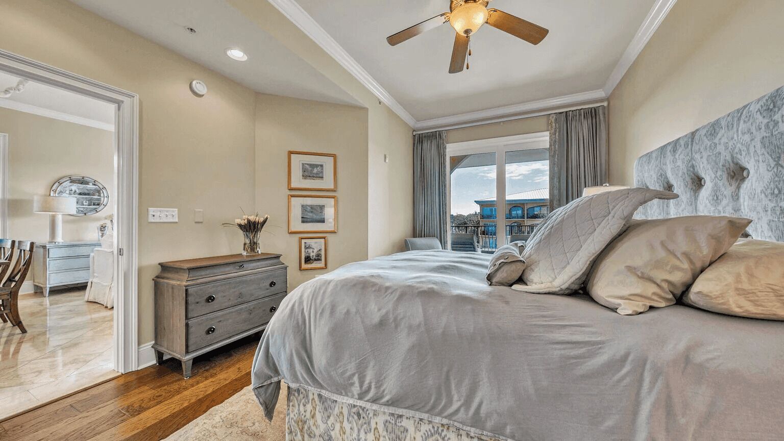 A bedroom with a bed, a dresser, a ceiling fan, and a window with a view.