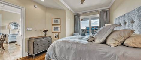 A bedroom with a bed, a dresser, a ceiling fan, and a window with a view.