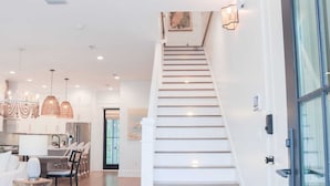 A modern interior with a staircase leading to a second floor, a dining area with a table and chairs, and pendant lighting. - Shellom by Avantstay Newly Built, Pool Access (Santa Rosa Beach)