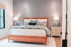 A bedroom with a wooden bed, patterned bedding, two bedside lamps, a nightstand, and a window with blinds. - Shellom by Avantstay Newly Built, Pool Access (Santa Rosa Beach)