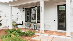 A white house with a covered porch, number 123, featuring a swing chair, wicker chairs, and hanging lanterns. - Shellom by Avantstay Newly Built, Pool Access (Santa Rosa Beach)