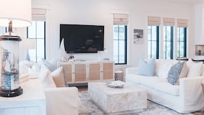 A living room with a white sofa, a coffee table, and a TV on the wall. - Shellom by Avantstay Newly Built, Pool Access (Santa Rosa Beach)