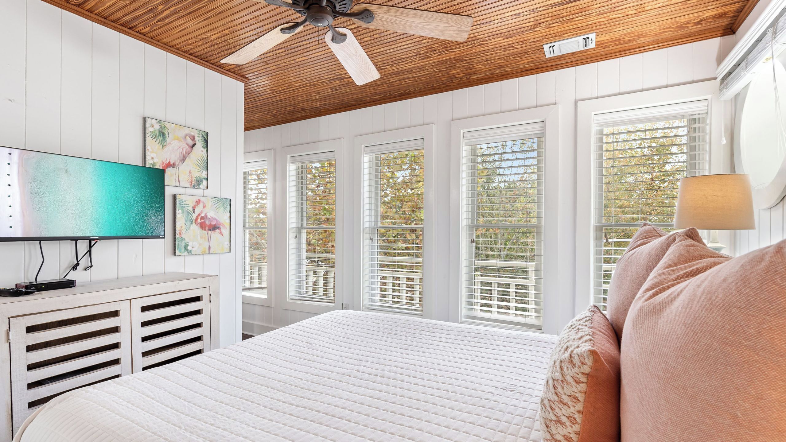 A bedroom with a bed, a ceiling fan, a TV, and artwork on the wall.