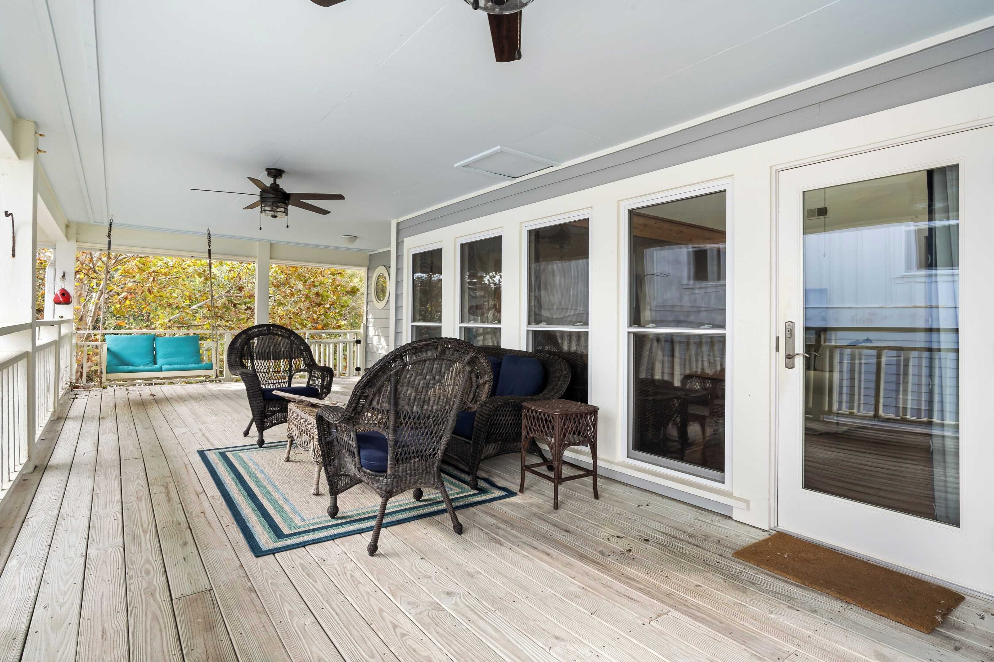A covered porch with wicker furniture, a ceiling fan, and large windows.