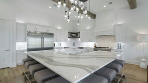Een moderne keuken met een groot eiland, roestvrijstalen apparatuur en hangende lampen.