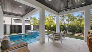 Ein überdachter Poolbereich im Freien mit Deckenventilator, einer Sitzecke mit Tisch und Blick auf den Garten.