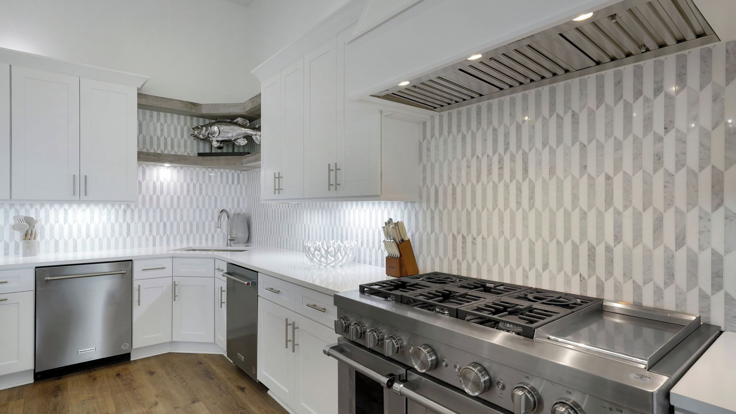 A modern kitchen with white cabinetry, a stainless steel stove, and a patterned backsplash.