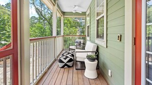 A covered porch with a white chair, a black and white ottoman, and a small table with a plant. - Bayou Bungalow by Avantstay Walk to Boat Ramp & Bay Private Yard (Santa Rosa Beach)