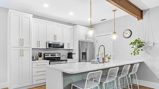 A modern kitchen with white cabinets, a central island with bar stools, stainless steel appliances, and pendant lighting. - Bayou Bungalow by Avantstay Walk to Boat Ramp & Bay Private Yard (Santa Rosa Beach)