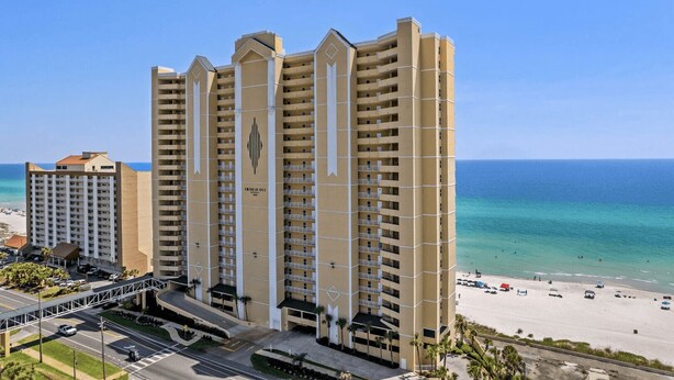 A high-rise hotel with multiple balconies, a beach view, and a pedestrian bridge connecting to the beach. - Emerald Isle 701 by Avantstay Gul Front Corner Unit 2 Pools (Panama City Beach)