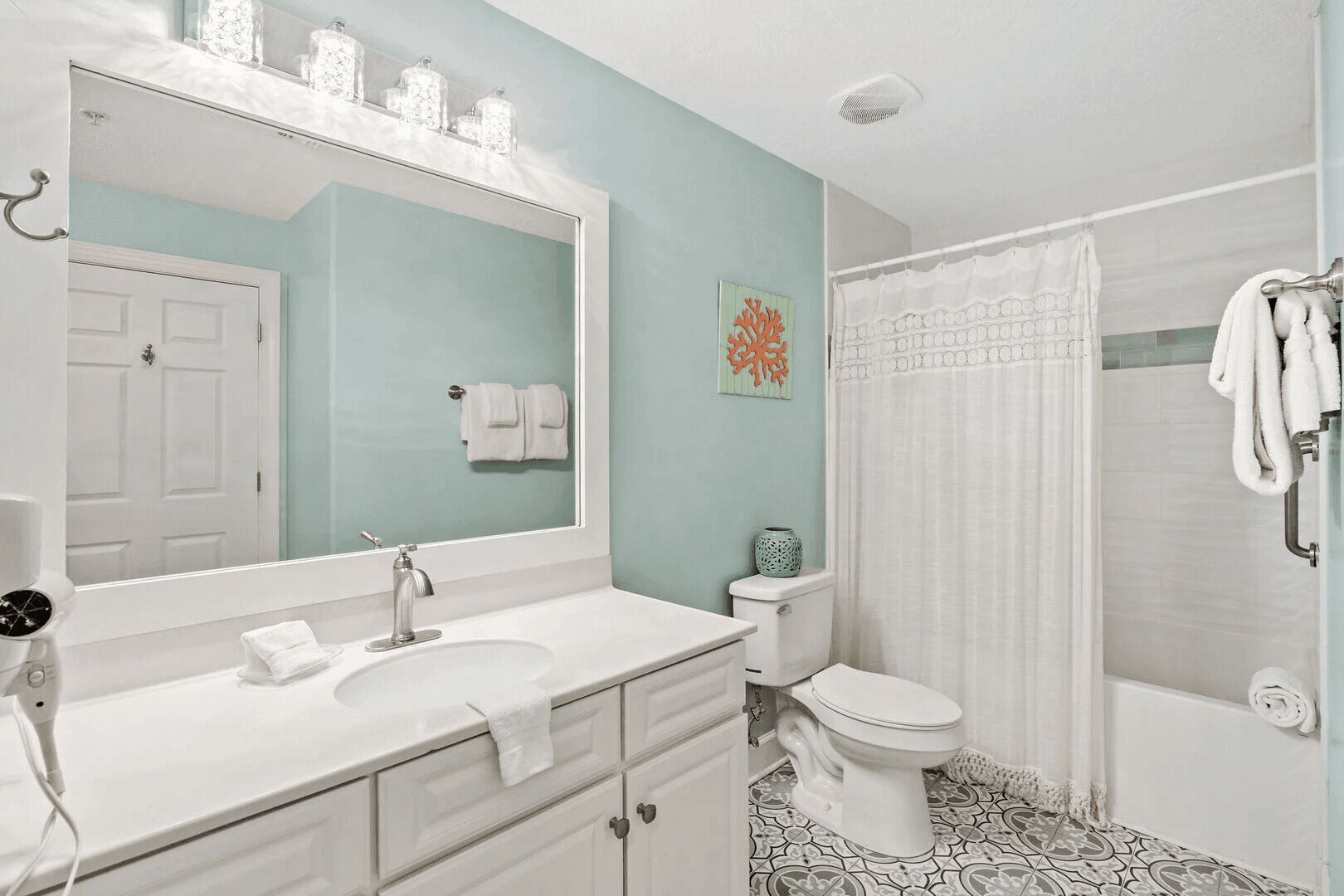 A bathroom with a white sink, mirror, and toilet. There is a shower curtain and a towel rack.