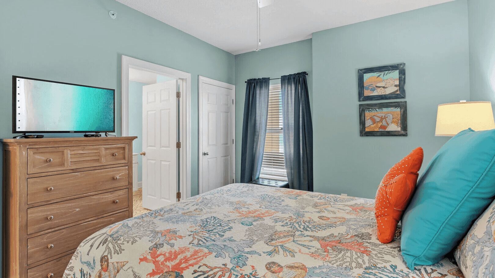 A bedroom with a bed, a dresser, a television, and a window with curtains.