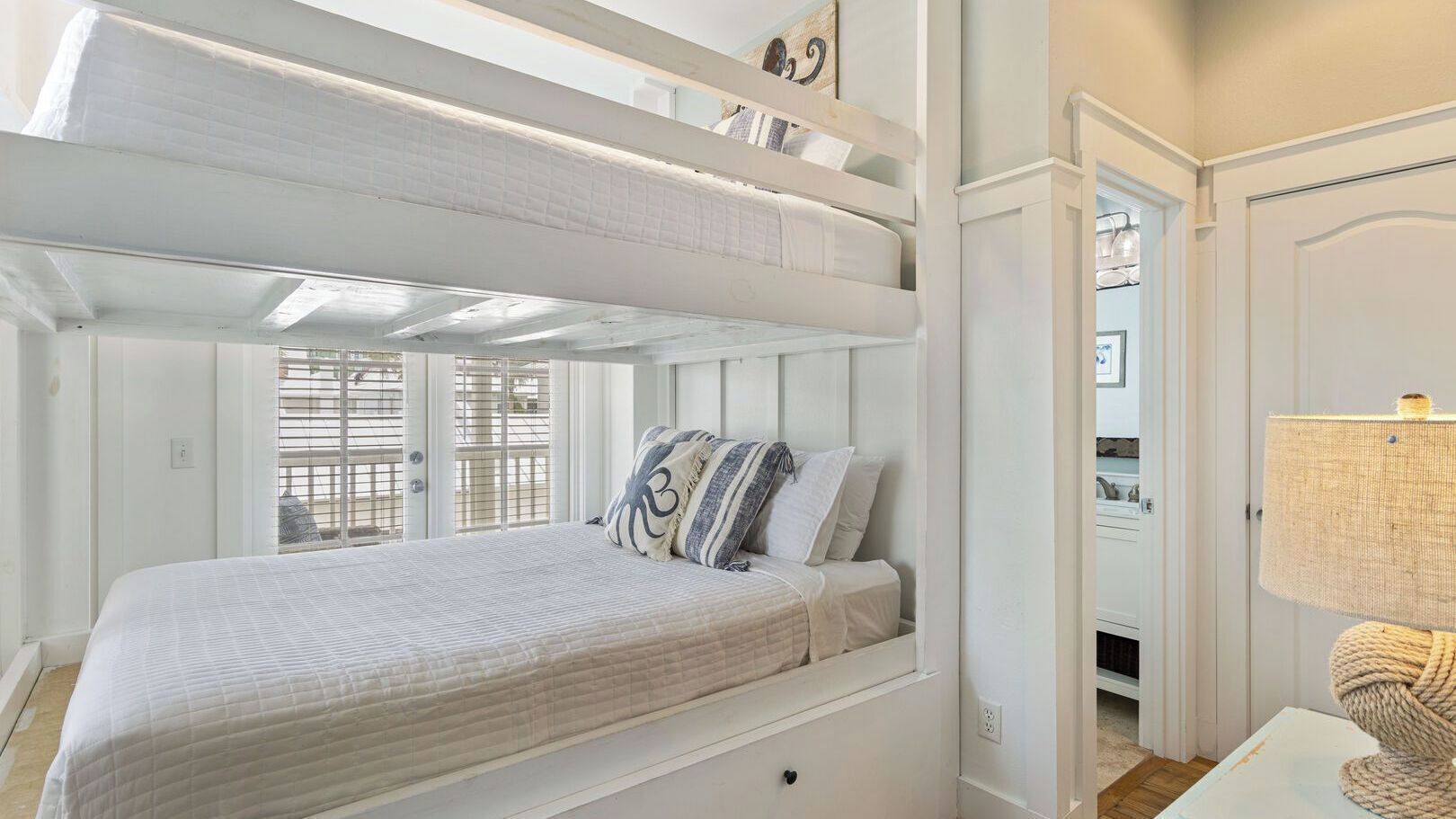 A bunk bed with a quilted mattress, striped pillows, and a lamp on a bedside table.
