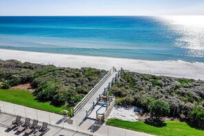 Vista sulla spiaggia con una passerella in legno che conduce alla riva, circondata da vegetazione lussureggiante.