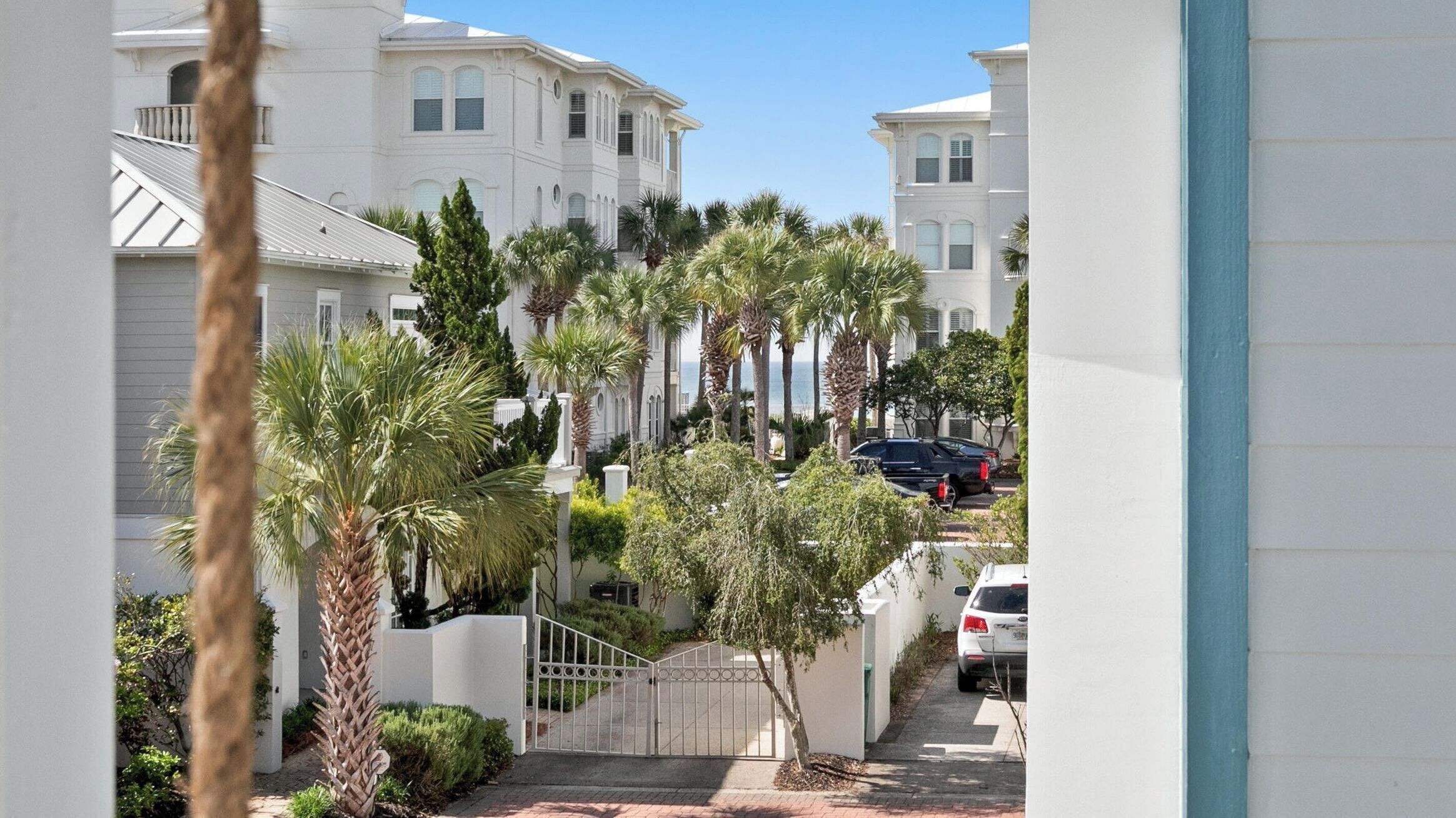 A residential street with white houses, palm trees, and parked cars.