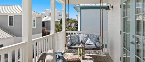 A covered porch with wicker furniture, a sofa with patterned cushions, and a lantern.