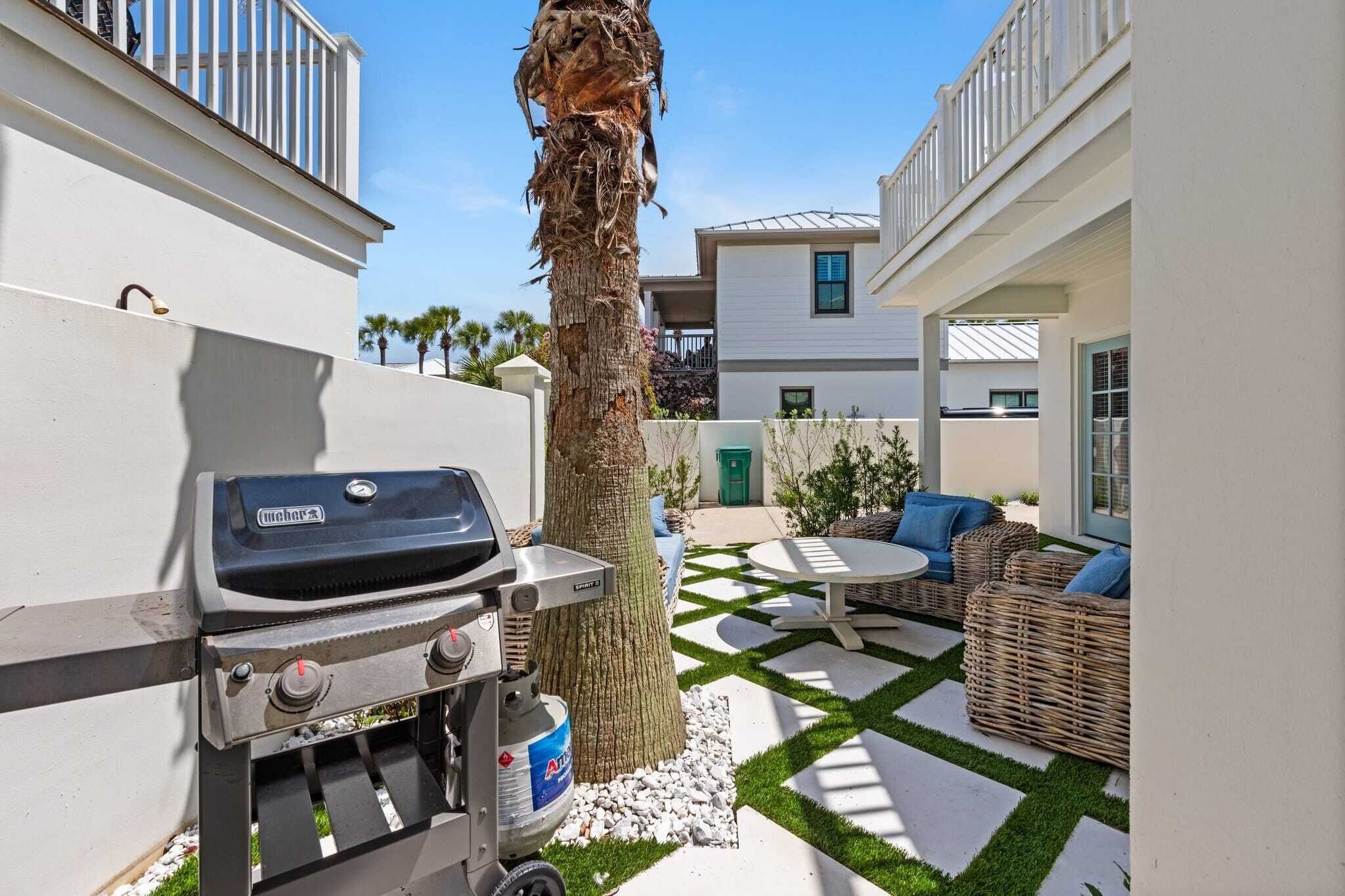 Un patio con una parrilla Weber, mobiliario de mimbre y una palmera.