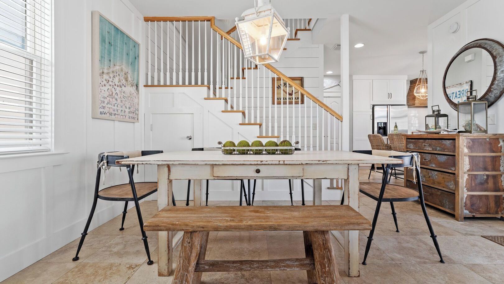 A dining area with a wooden table, benches, and a staircase with white railings.