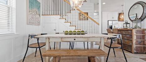 A dining area with a wooden table, benches, and a staircase with white railings.