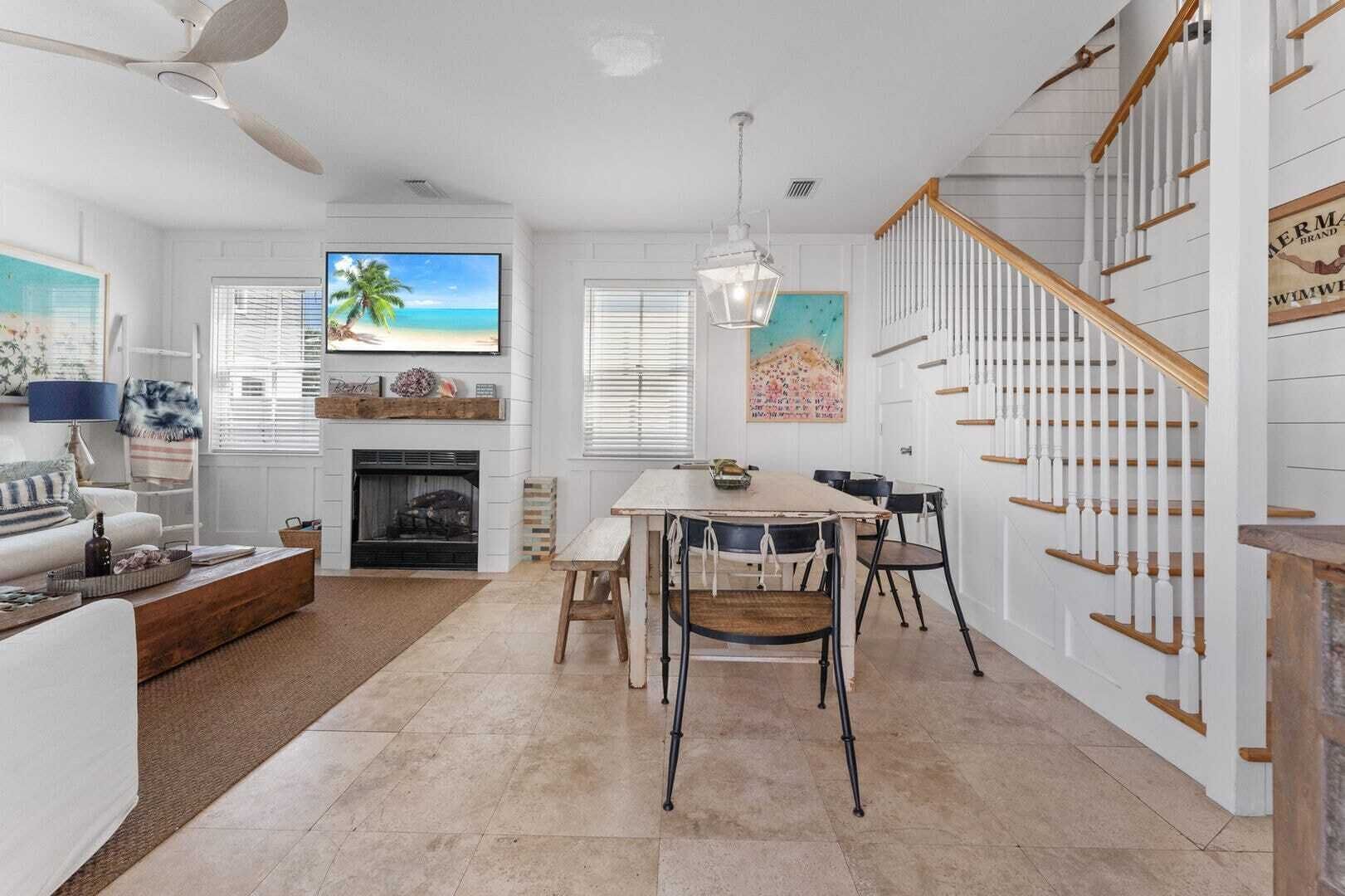 A spacious living room with a fireplace, a dining area with a table and chairs, and a staircase with wooden railings.