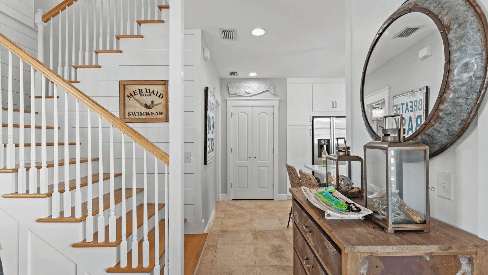 A staircase with wooden steps and white railings, a hallway with a wooden dresser, a mirror, and a door with a sign.