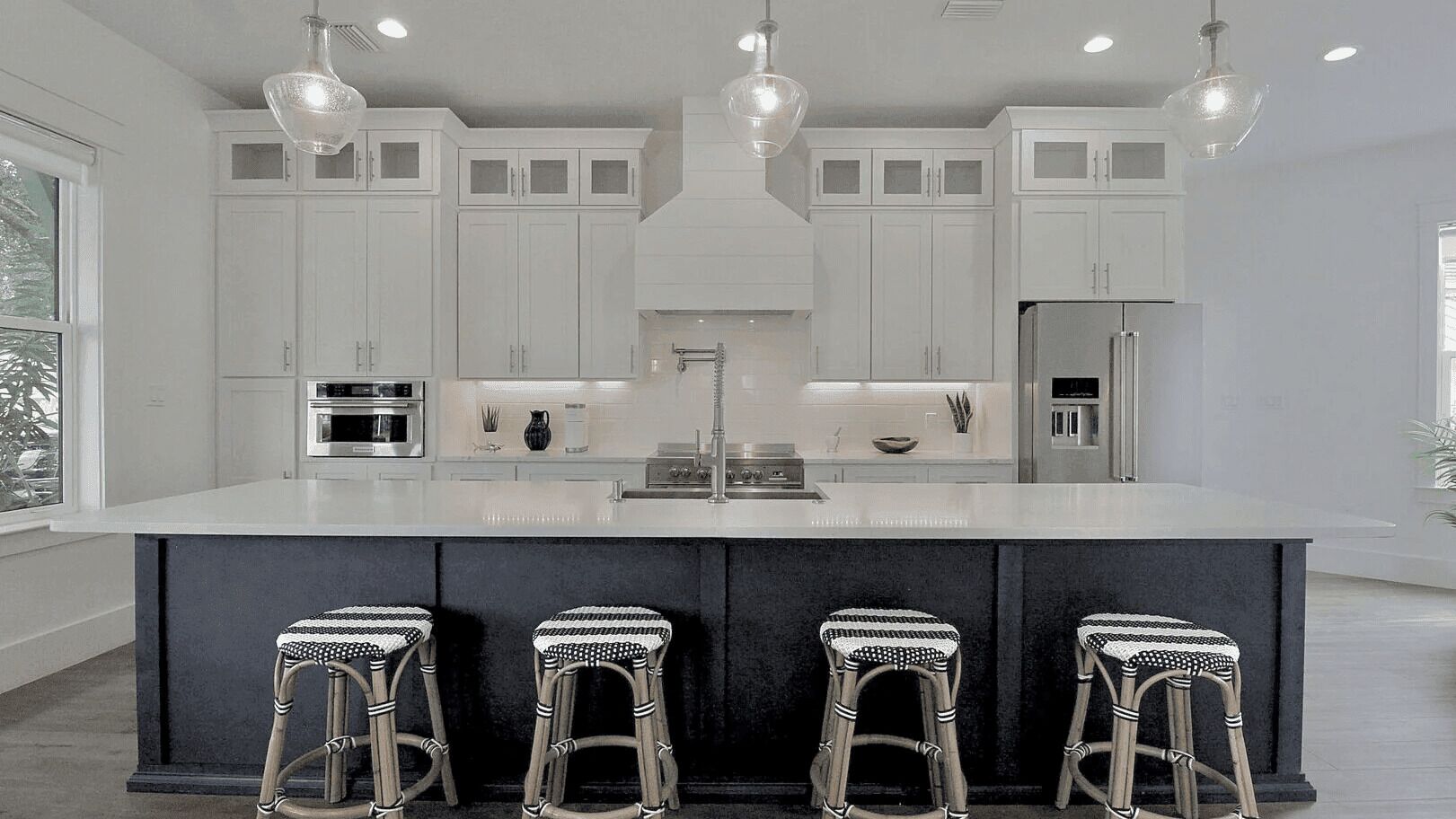 Una cocina moderna con armarios blancos, una isla central, taburetes de bar e iluminación colgante.