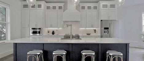 Una cocina moderna con armarios blancos, una isla central, taburetes de bar e iluminación colgante.